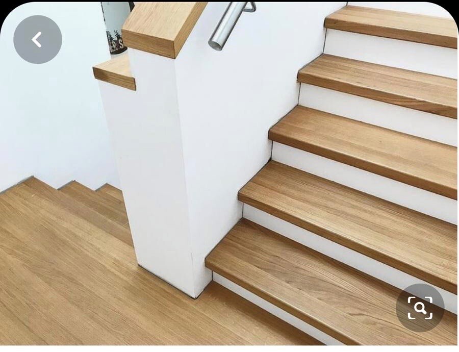 Interior staircase with wooden steps, white walls and a central wall between two flights of stairs.