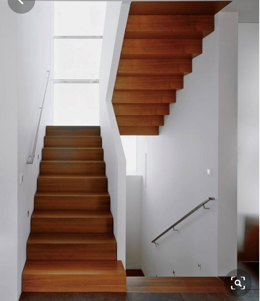 Modern indoor staircase made of dark wood, L-shaped staircase with two sections and white walls.