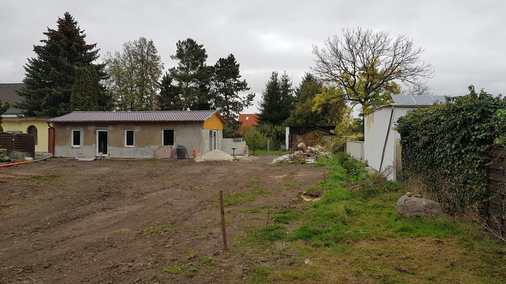Unfinished building site with soil, sand piles, and trees in the background.