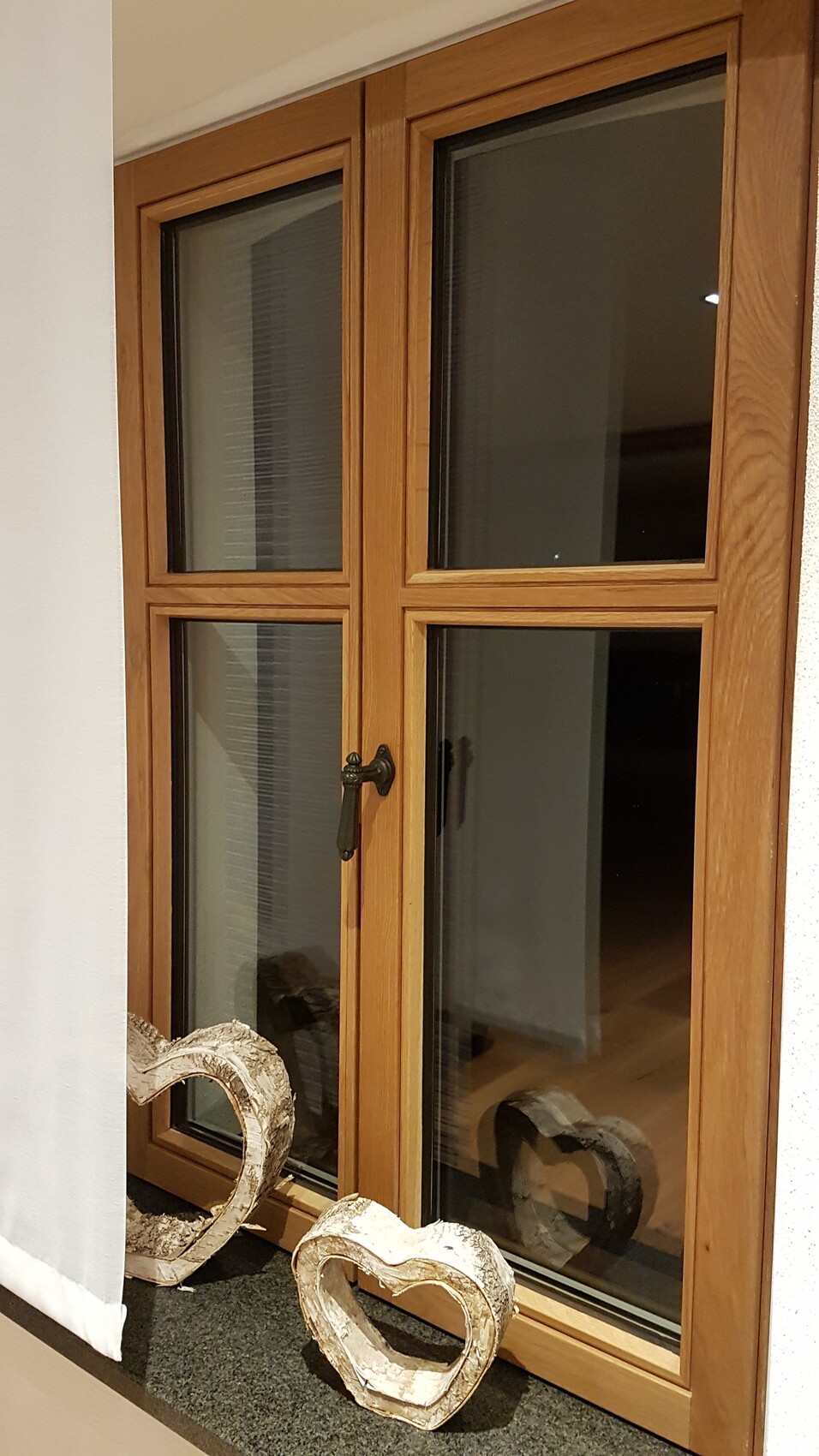 Holz-Doppelfenster-Tür mit vier Glasfeldern; zwei weiße Herz-Dekofiguren liegen davor.