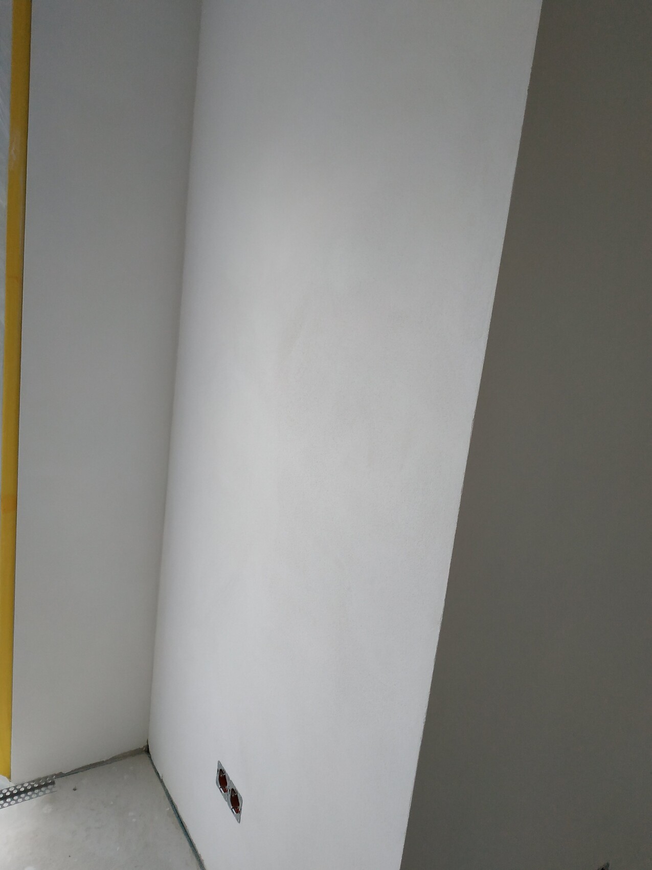 White interior wall with a round column in the corner; construction area with open cable outlet at the floor.