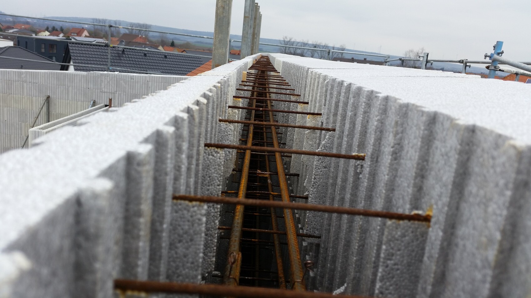 View through an excavation pit with rusty reinforcement bars between concrete blocks.