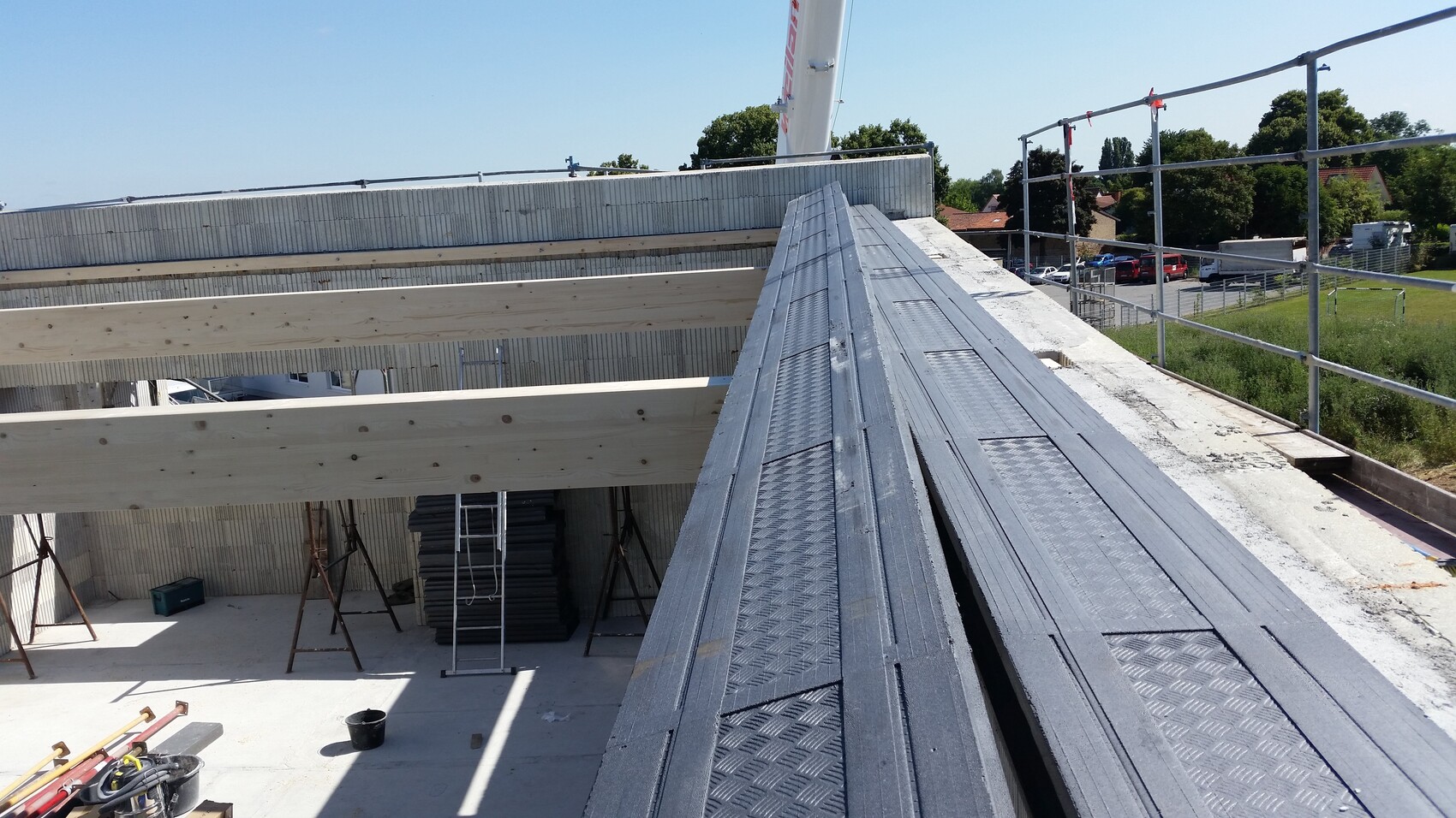 Roof construction site with metal sheets and wooden beams, scaffolding at the edge, view of houses and streets.