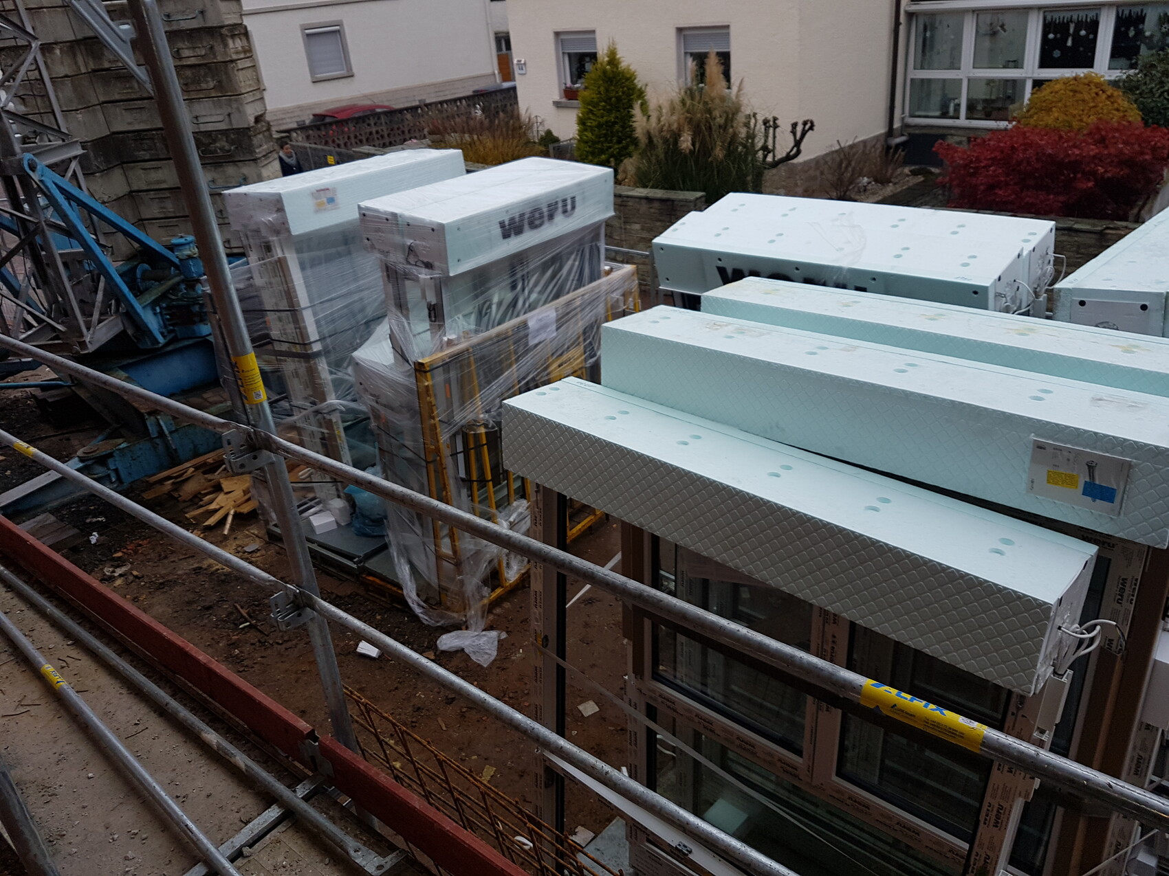 Construction site with scaffolding, insulation panels, and building materials on the plot.