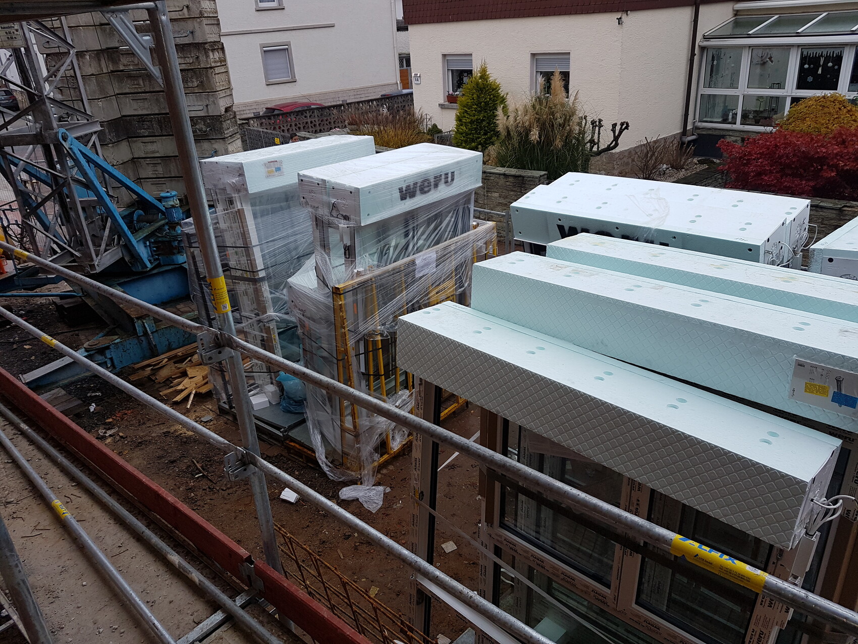 Baustelle mit gestapelten Dämmplatten, Fensterrahmen und Gerüst