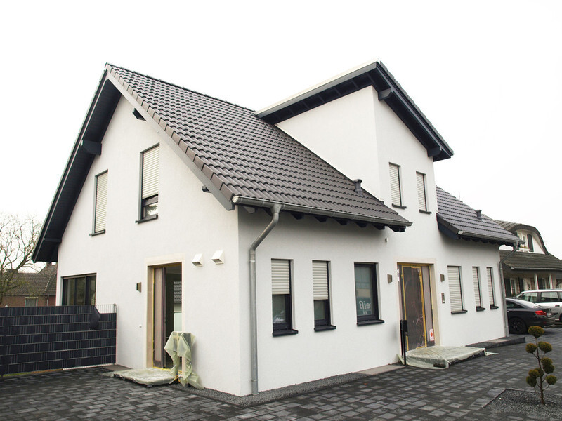 Modern white two-story single-family house with dark tiled roof and paved driveway