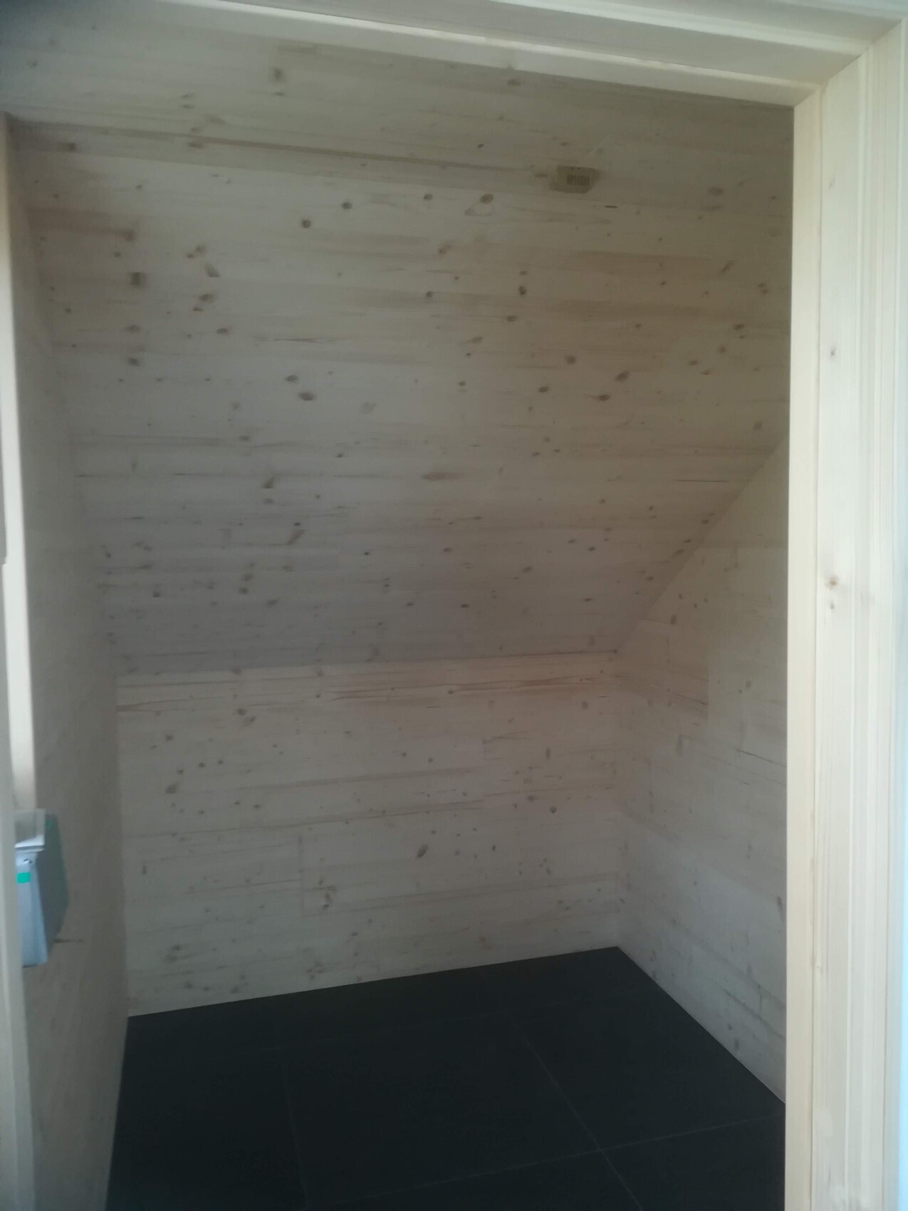 Empty room with light wood-paneled walls and dark tiled floor.