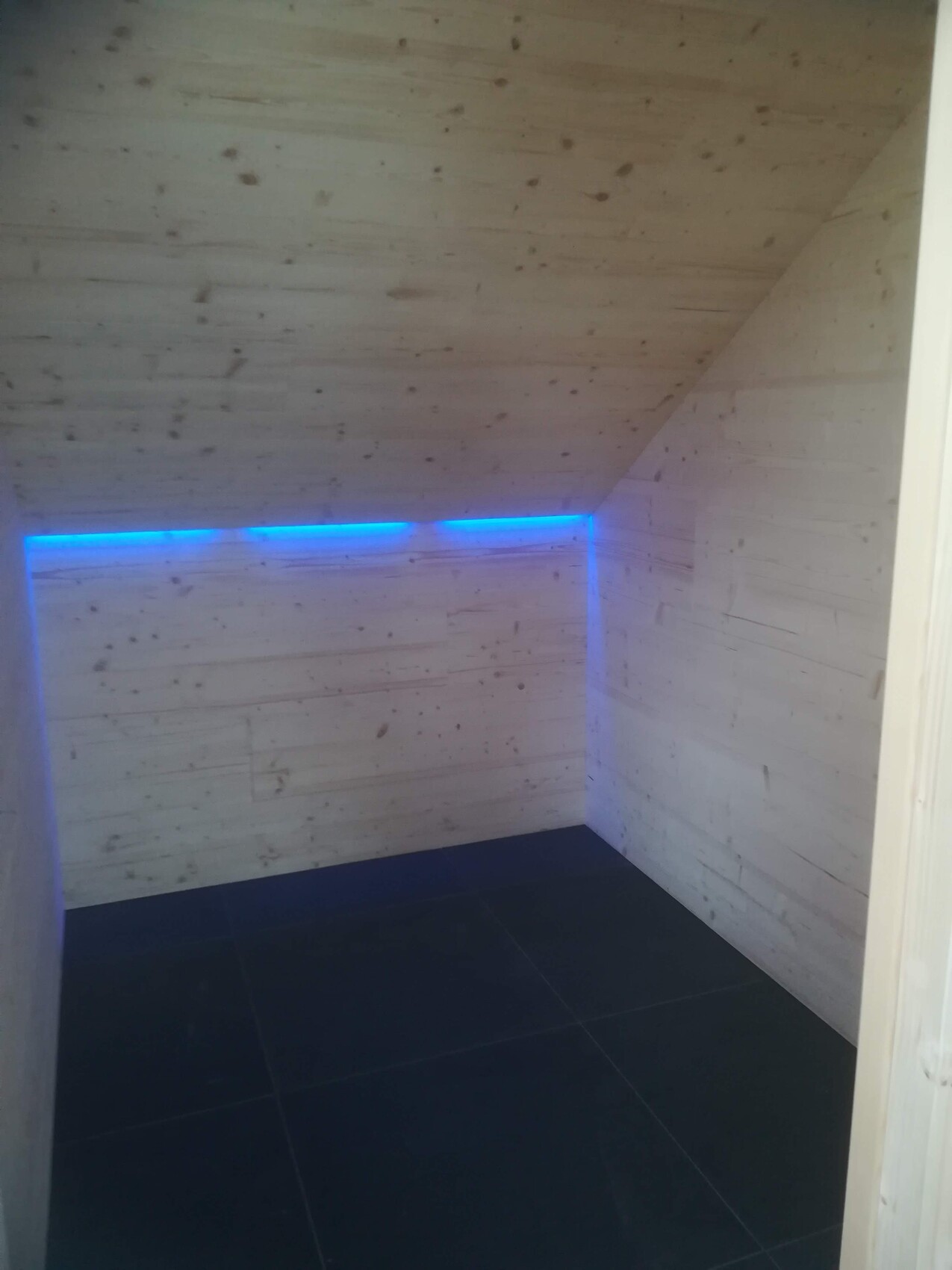 Small room with wood paneling, blue LED light strip along the corner, dark floor.