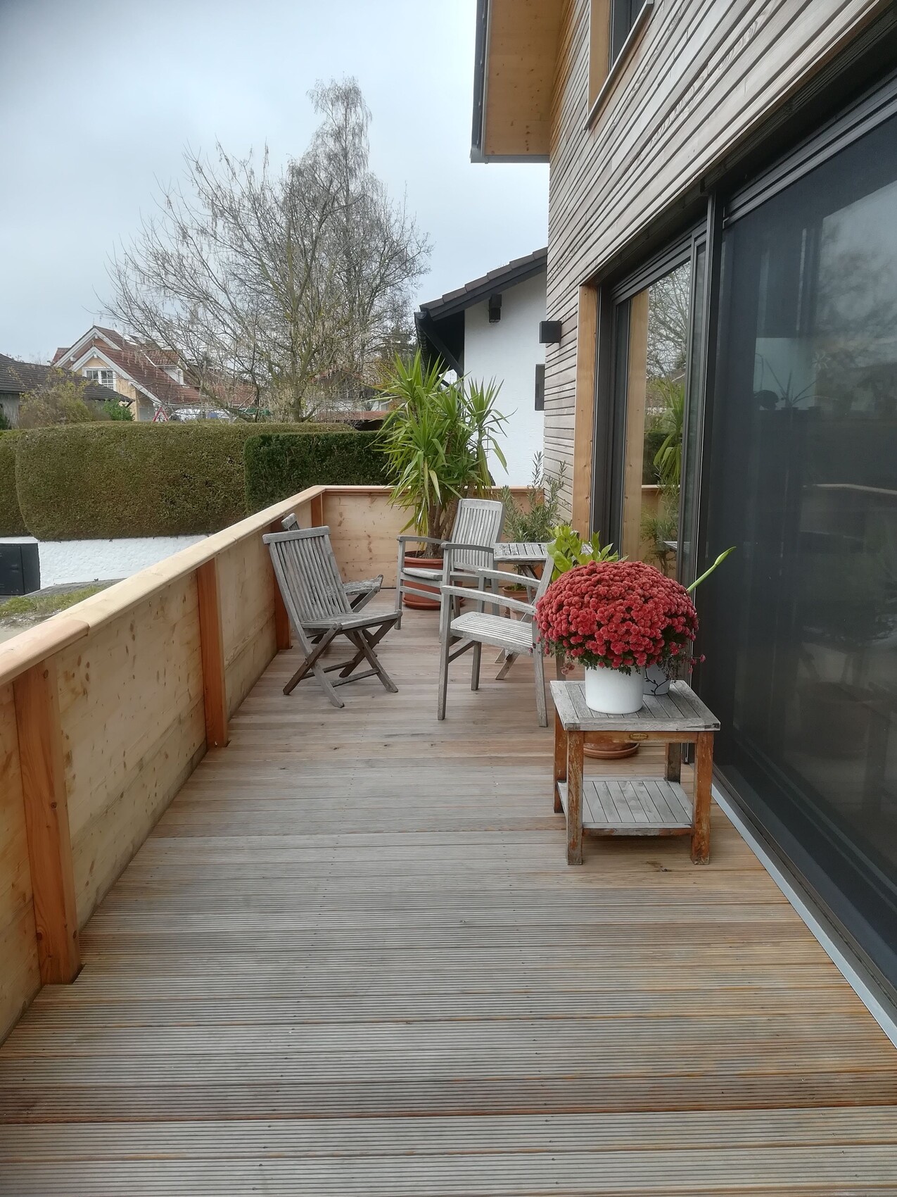 Wooden terrace with balcony furniture, plant pot, and glass sliding door.