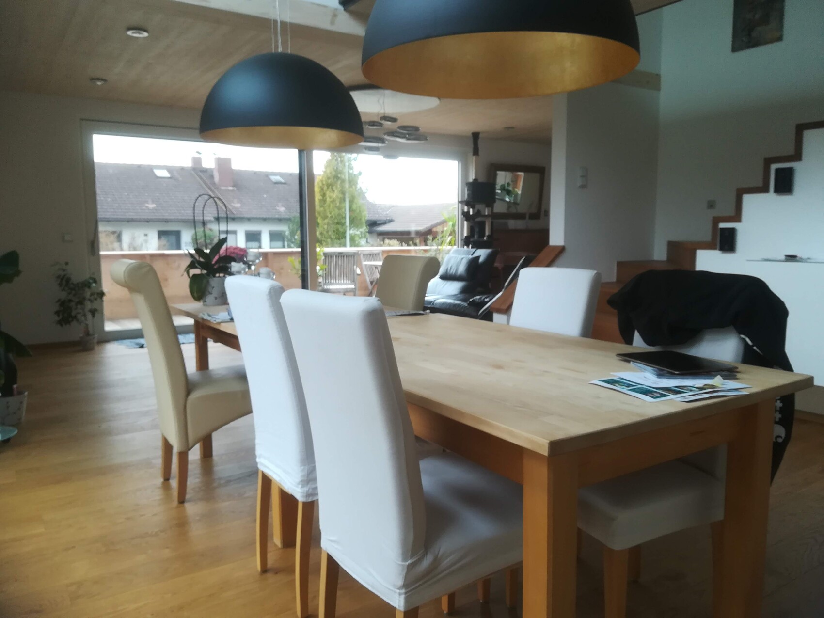Bright dining room with wooden table and white chairs, dark pendant lamps; balcony visible.