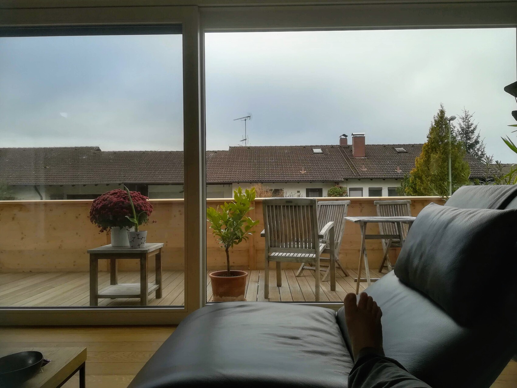 Living room with balcony view: black leather sofa in the foreground, foot visible, table set and plants.