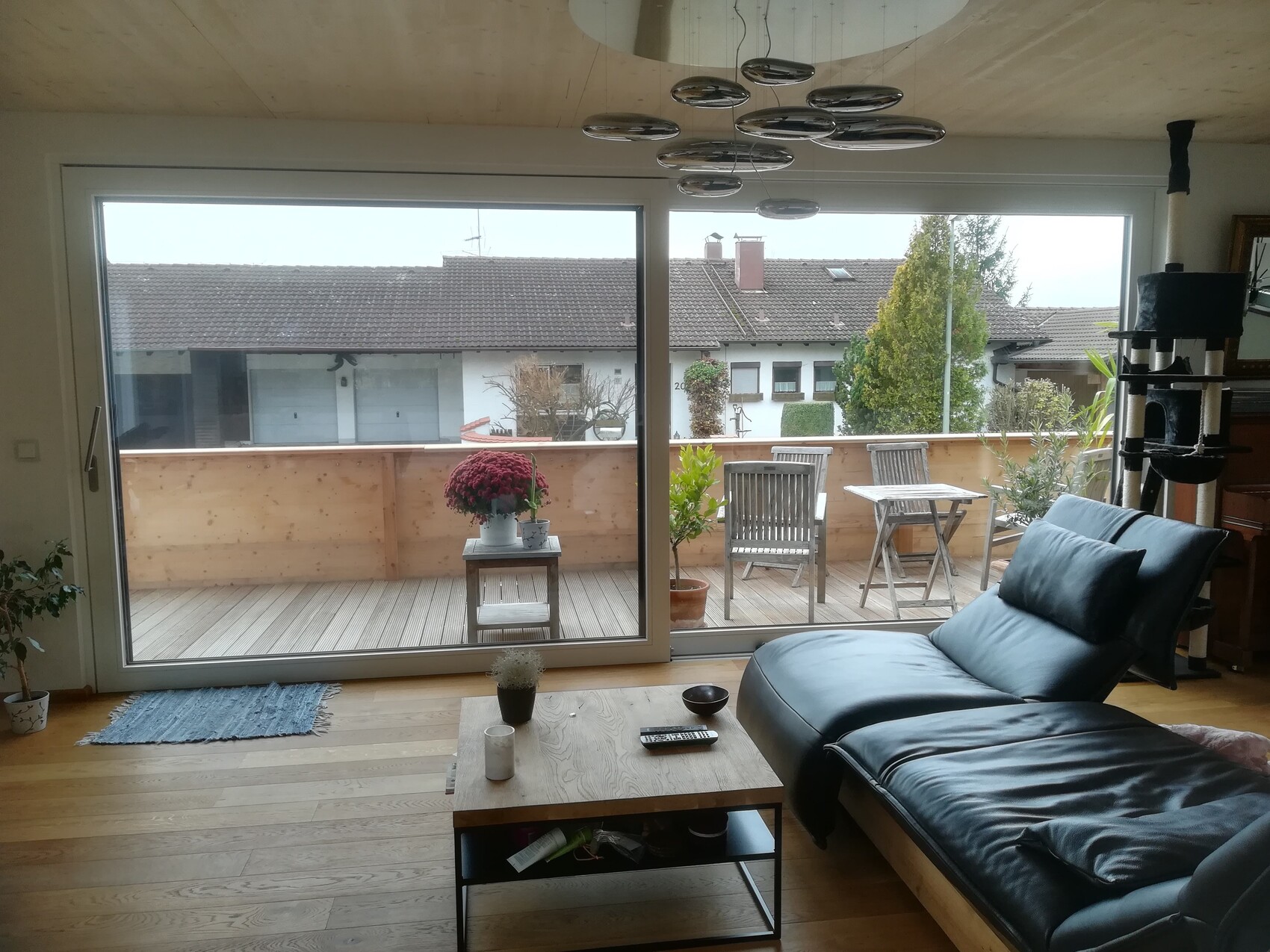 Living room with large glass sliding door to the terrace, leather sofa, wooden table, and balcony furniture.