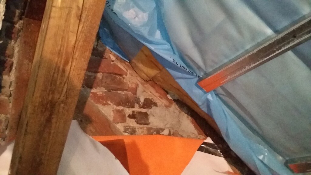 Construction site with brick wall, wooden beams, and blue protective foil during interior construction.