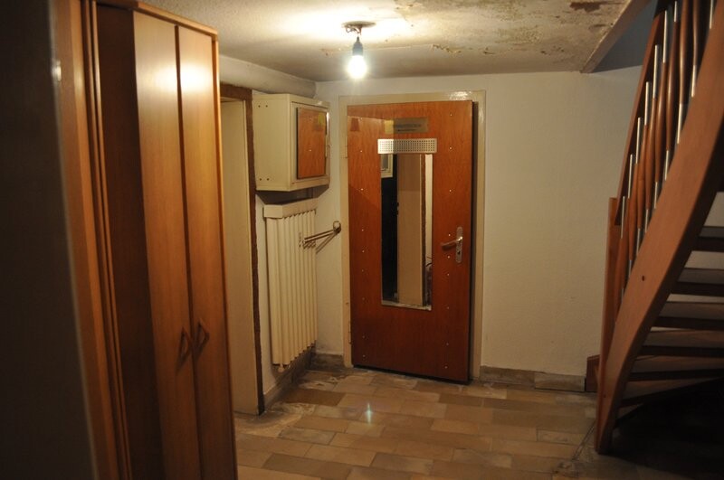 Basement hallway with wooden doors on the left, radiator, staircase on the right, and light bulb on the ceiling.