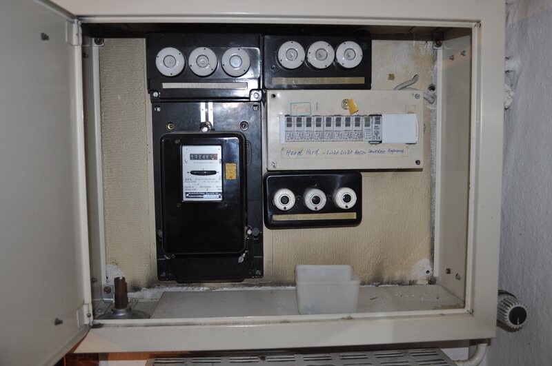 Old electrical distribution box with meters, fuses, and indicators in a wall niche.