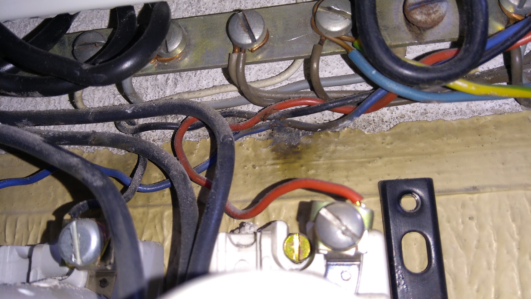 Wiring behind a metal strip with screws, dust, and colored cables.
