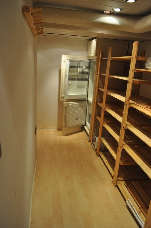 Narrow storage room with wooden shelves on the right and small refrigerator at the back.