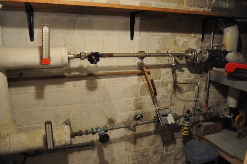 Basement heating room with piping, valves, thermometers, and measuring device.