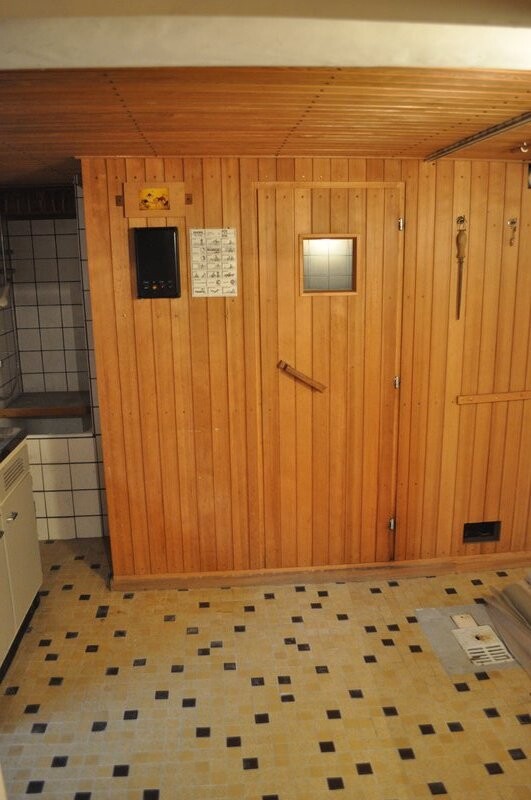 Sauna room made of wood with door, small window, instructions on the wall, and tiled floor.
