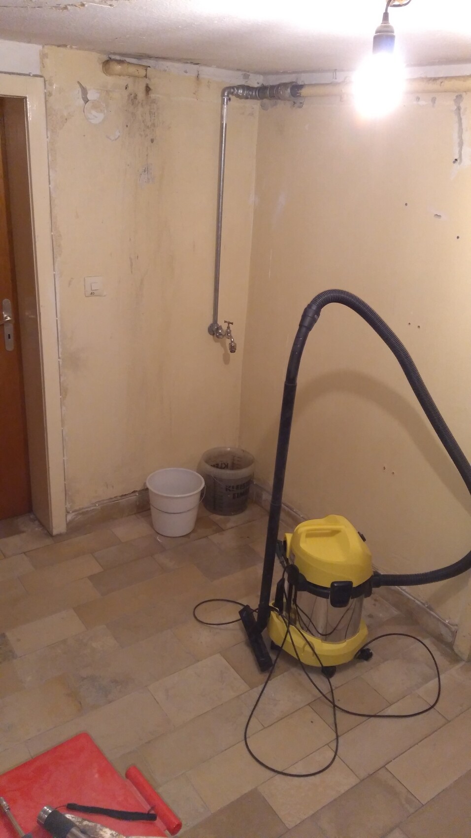 Basement room with yellow wet/dry vacuum cleaner, flexible hose, two buckets, and wall pipes.