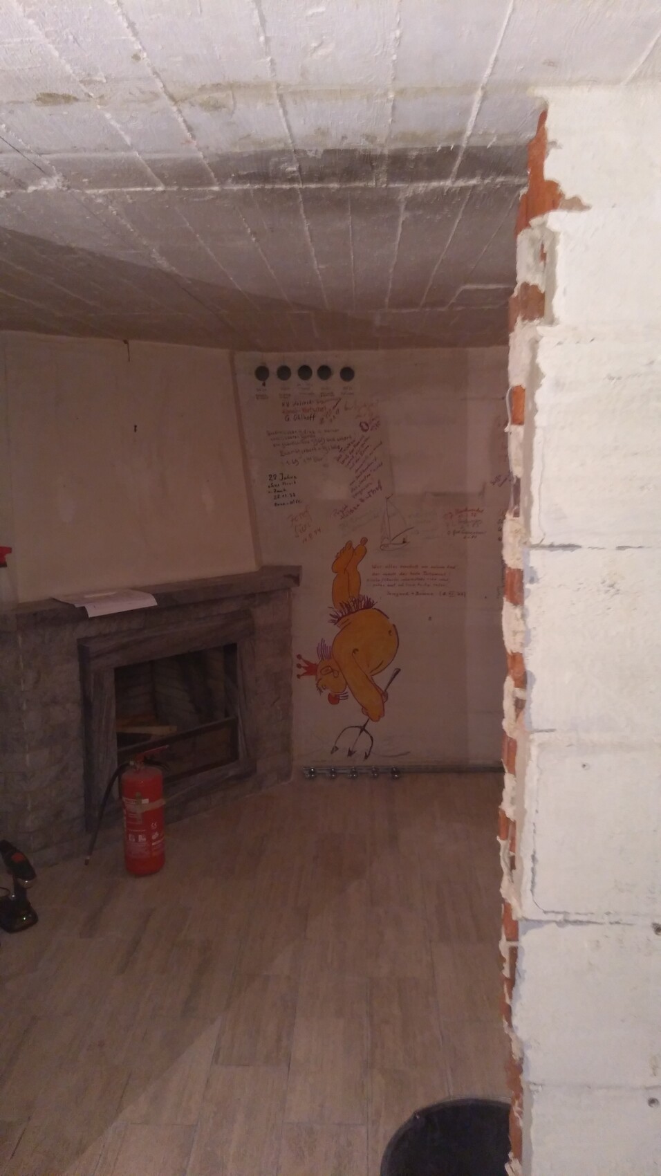 Basement room with fireplace, red fire extinguisher, and wall painting of a yellow cartoon chicken.