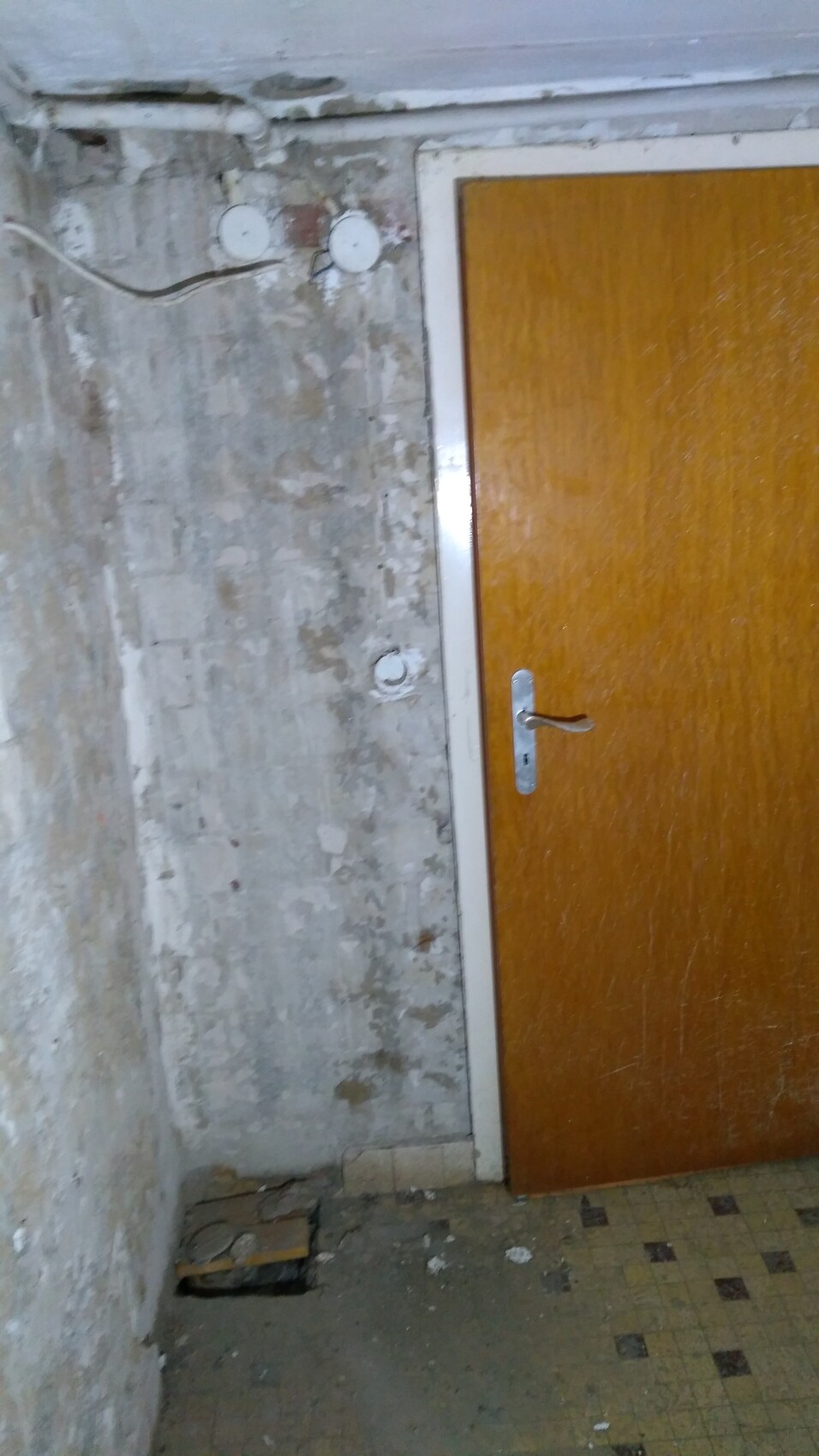 Abandoned room with wooden door, rough plaster wall, cables, and debris.