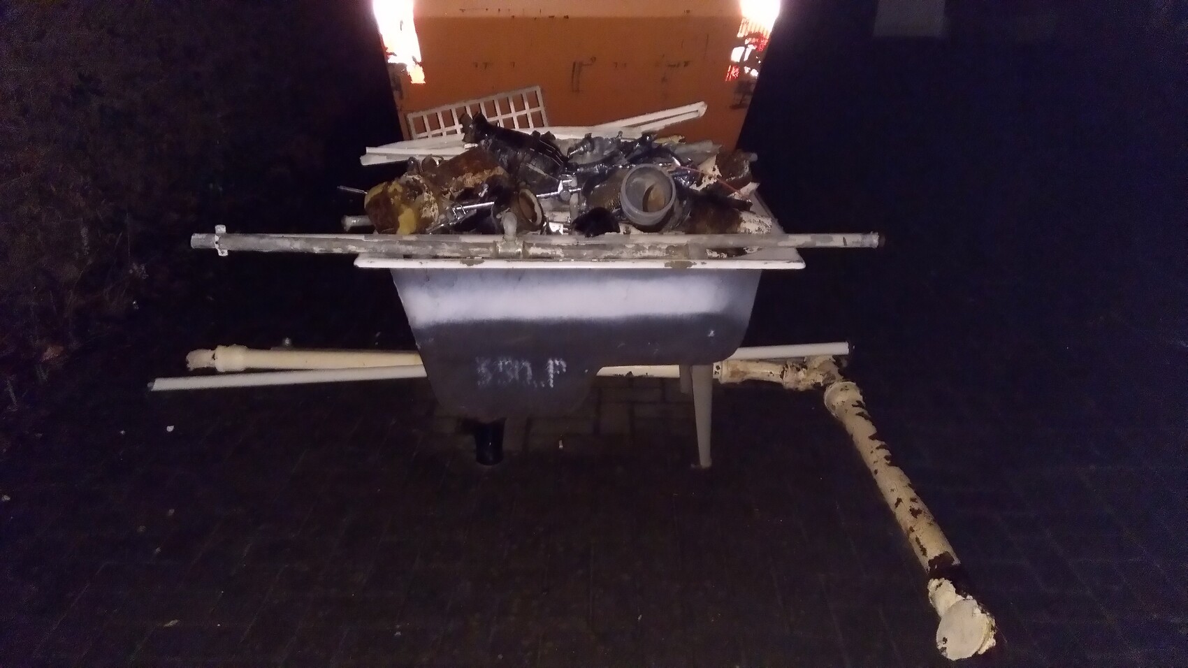 Night shot: trash and metal parts loaded on a wheelbarrow, dark background.