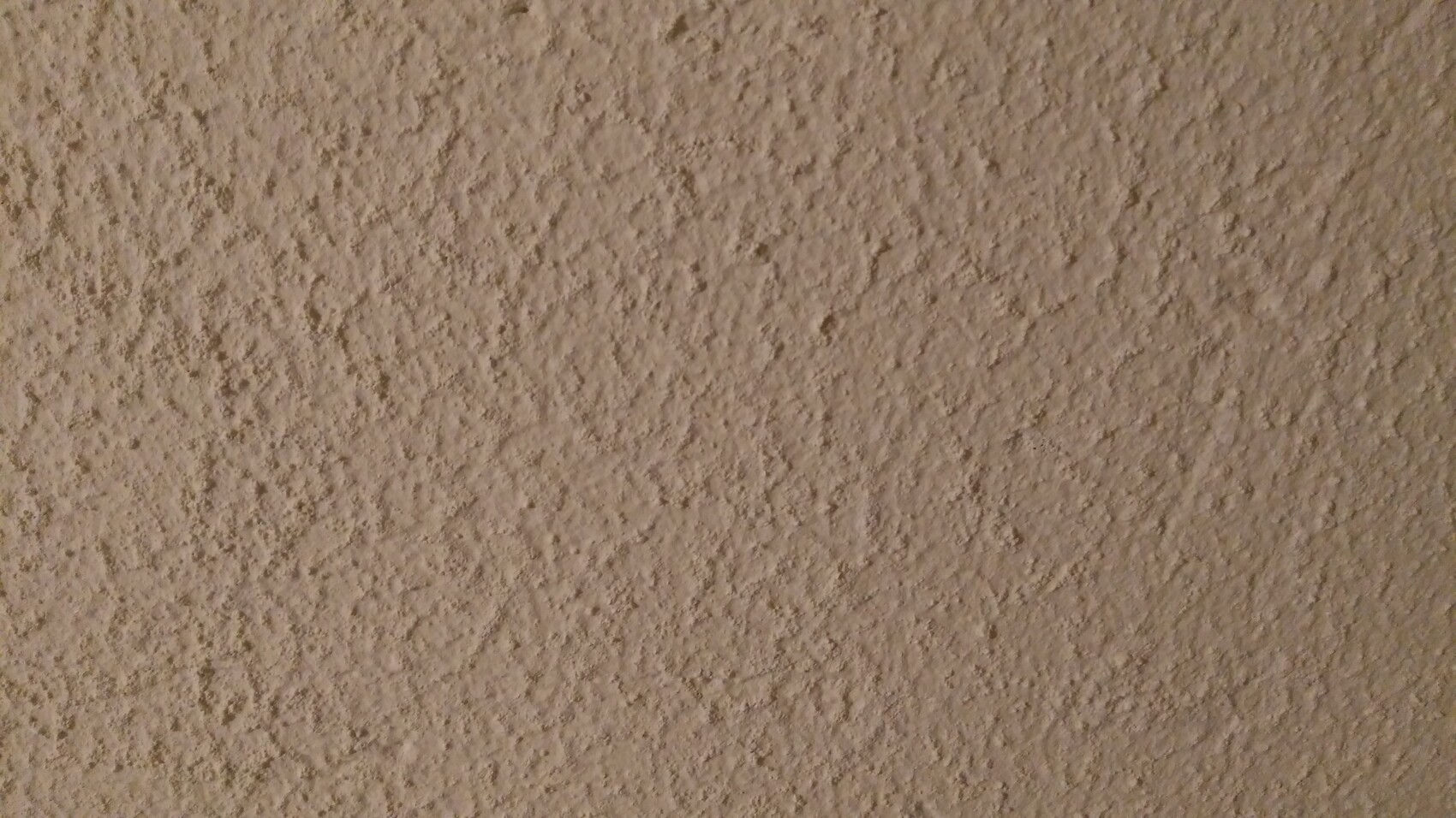 Close-up of a rough, beige plaster wall with coarse texture.