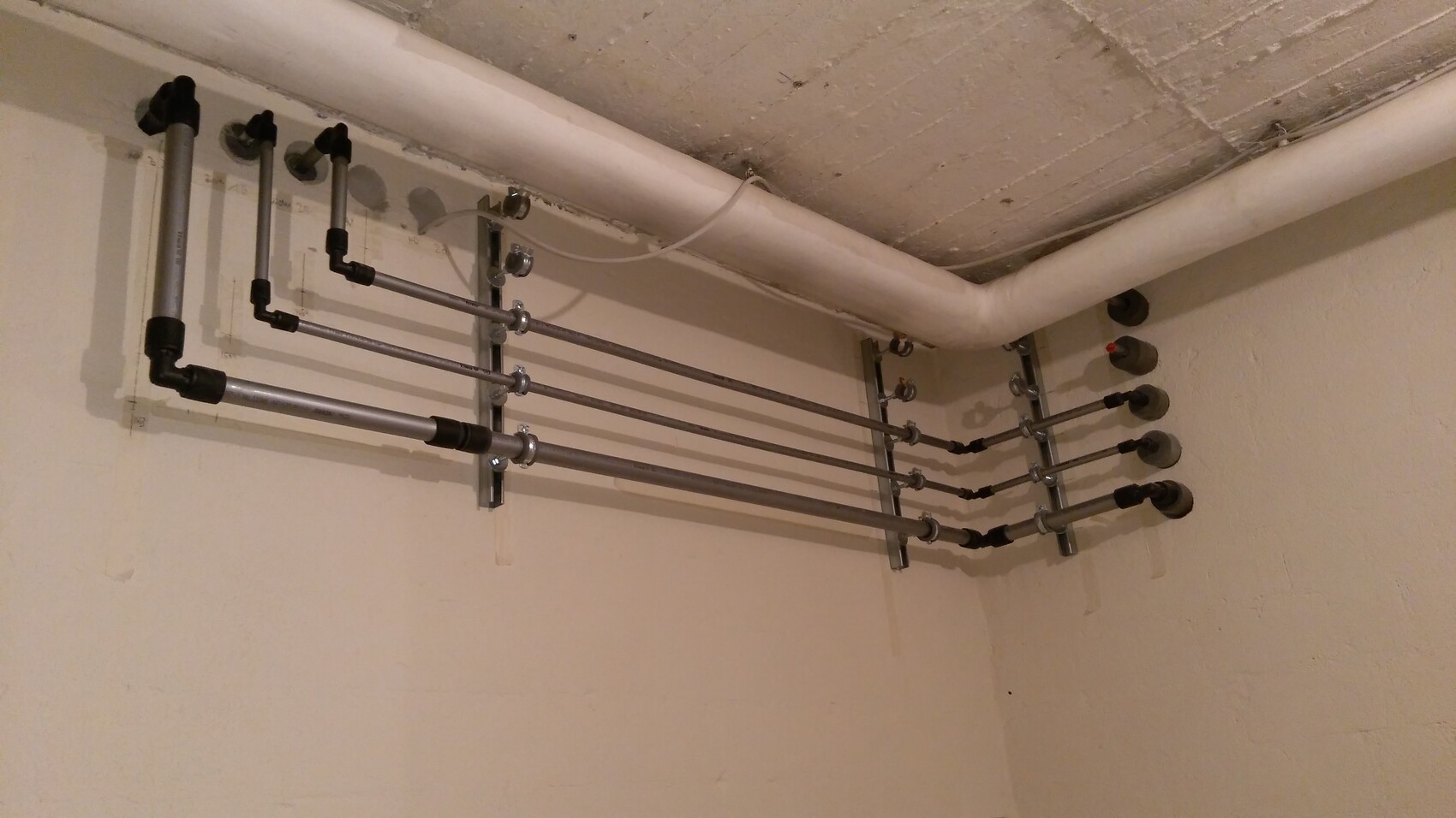 Basement pipe installation: multiple parallel metal pipes mounted on brackets and one PVC pipe.