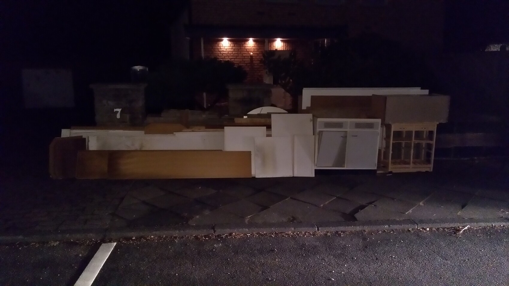 Night shot: bulky waste on the roadside, wood panels, doors, and refrigerator placed there.