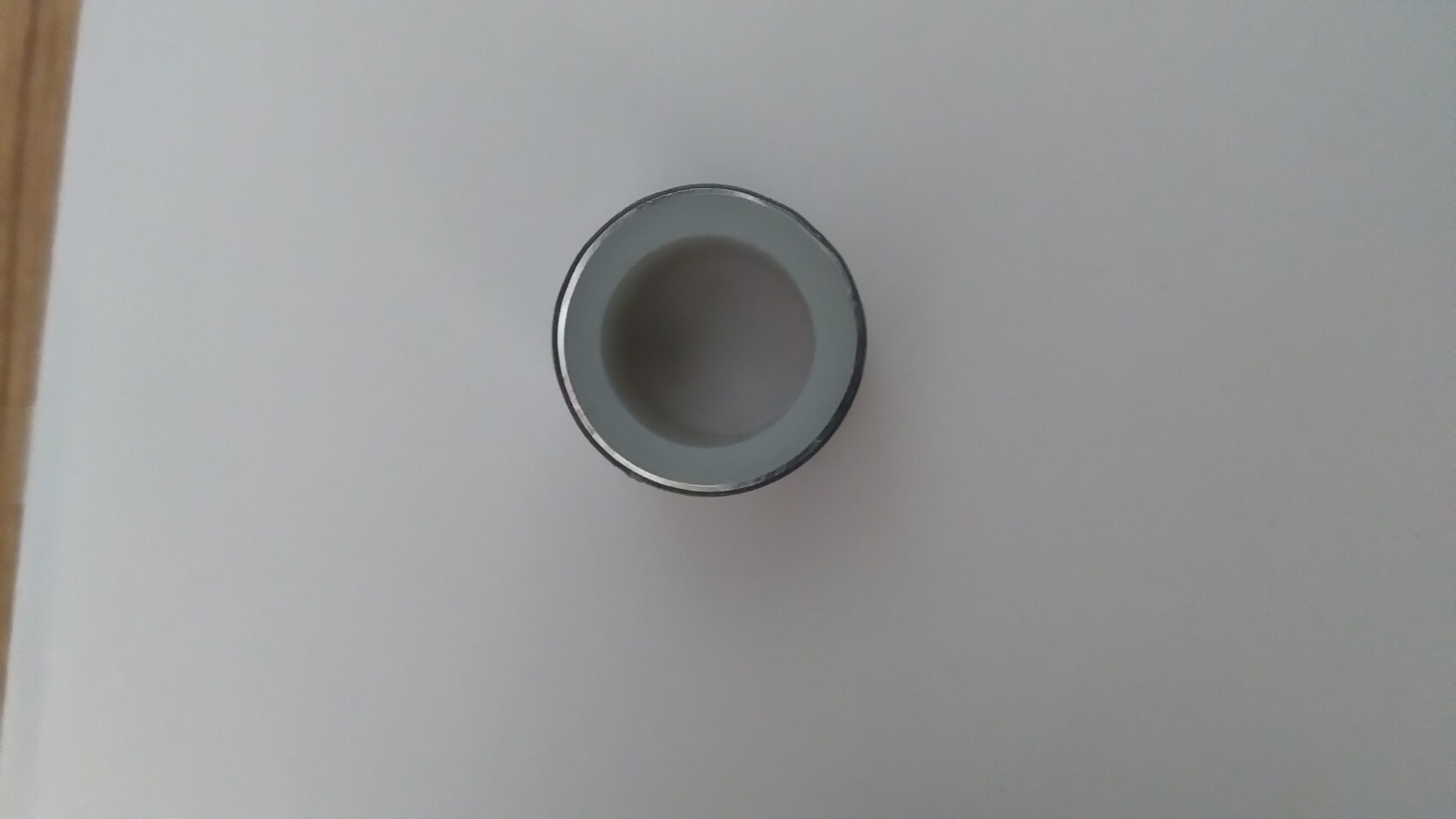 Empty silver metal cup viewed from above, round opening, lying on a light-colored table.
