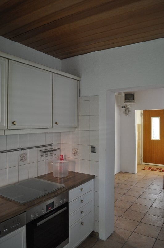 Kitchen with white wall cabinets, stove, wooden countertop, and passage to the hallway.