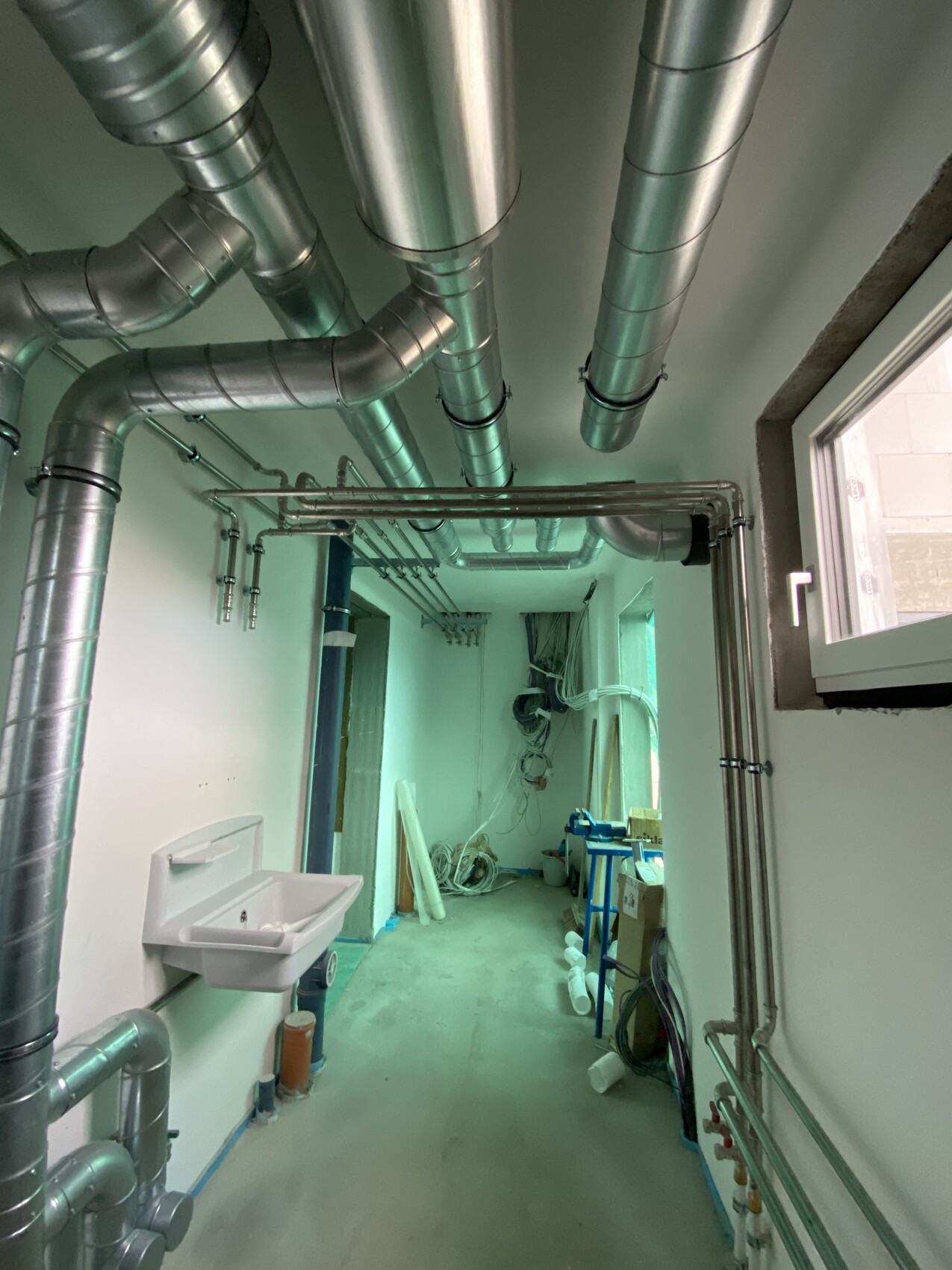 Technikraum mit vielen Metallrohren, Spüle links, Kabel und Werkzeuge, Fenster rechts