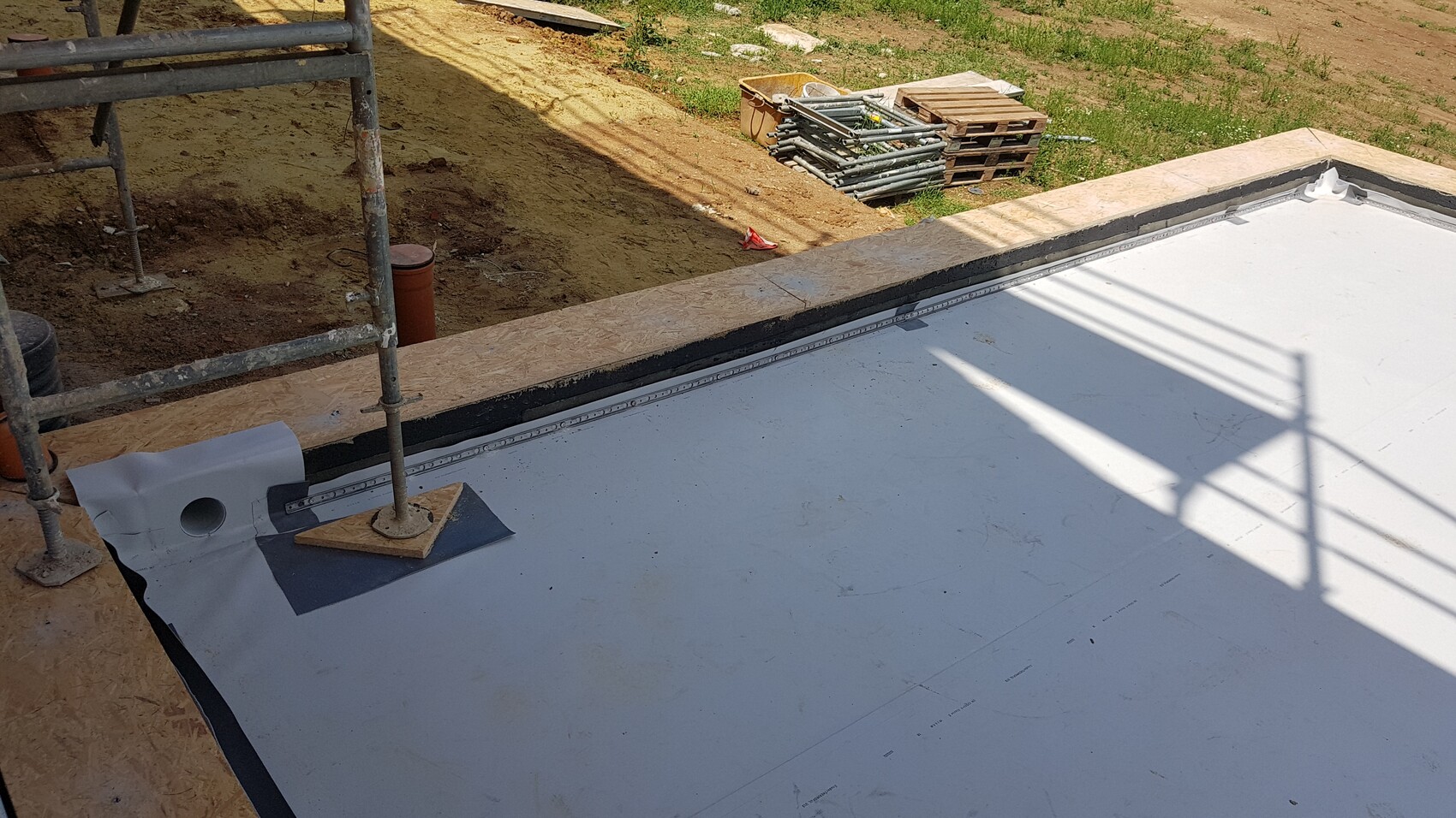 Construction site: white, flat substrate with black sealing membrane, scaffolding and pallets.