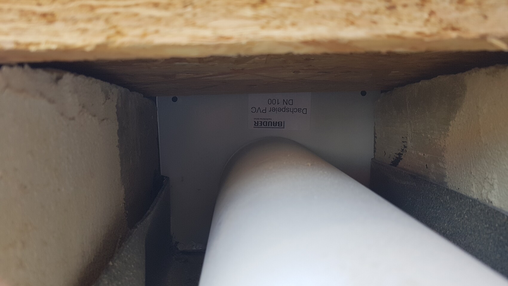 Close interior view of a PVC elbow (90°) behind wooden panel and wall.