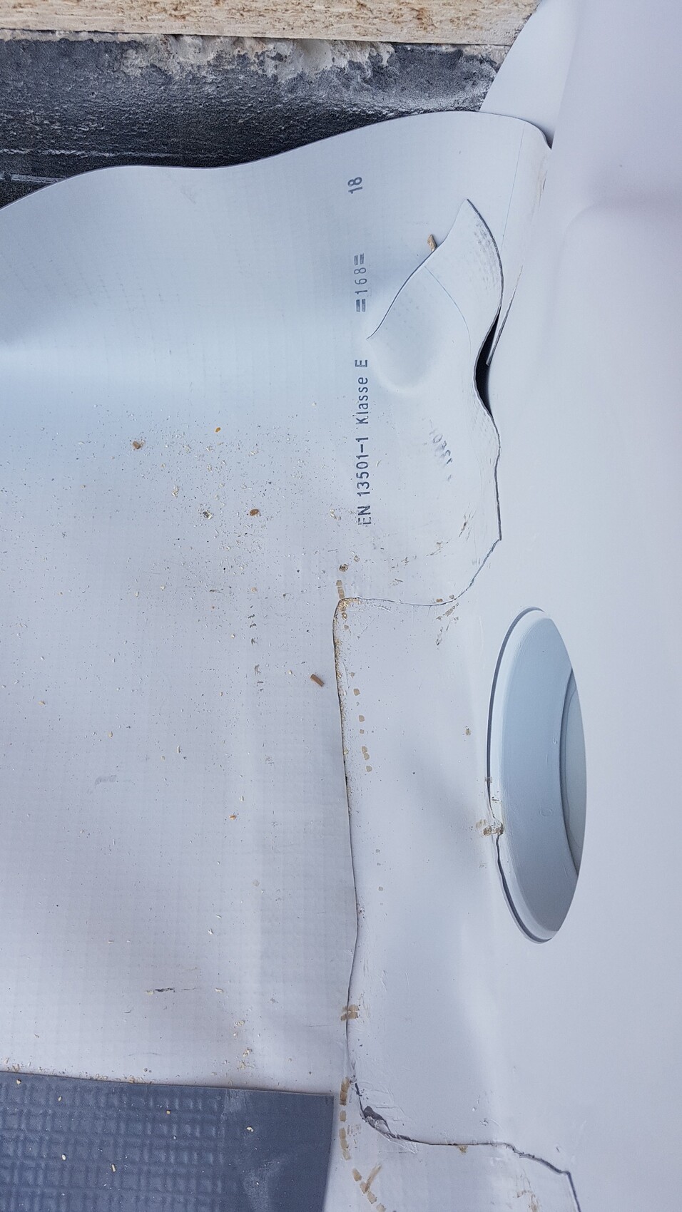 Damaged white cladding with crack and round blind panel; EN 13501-1 Class E.