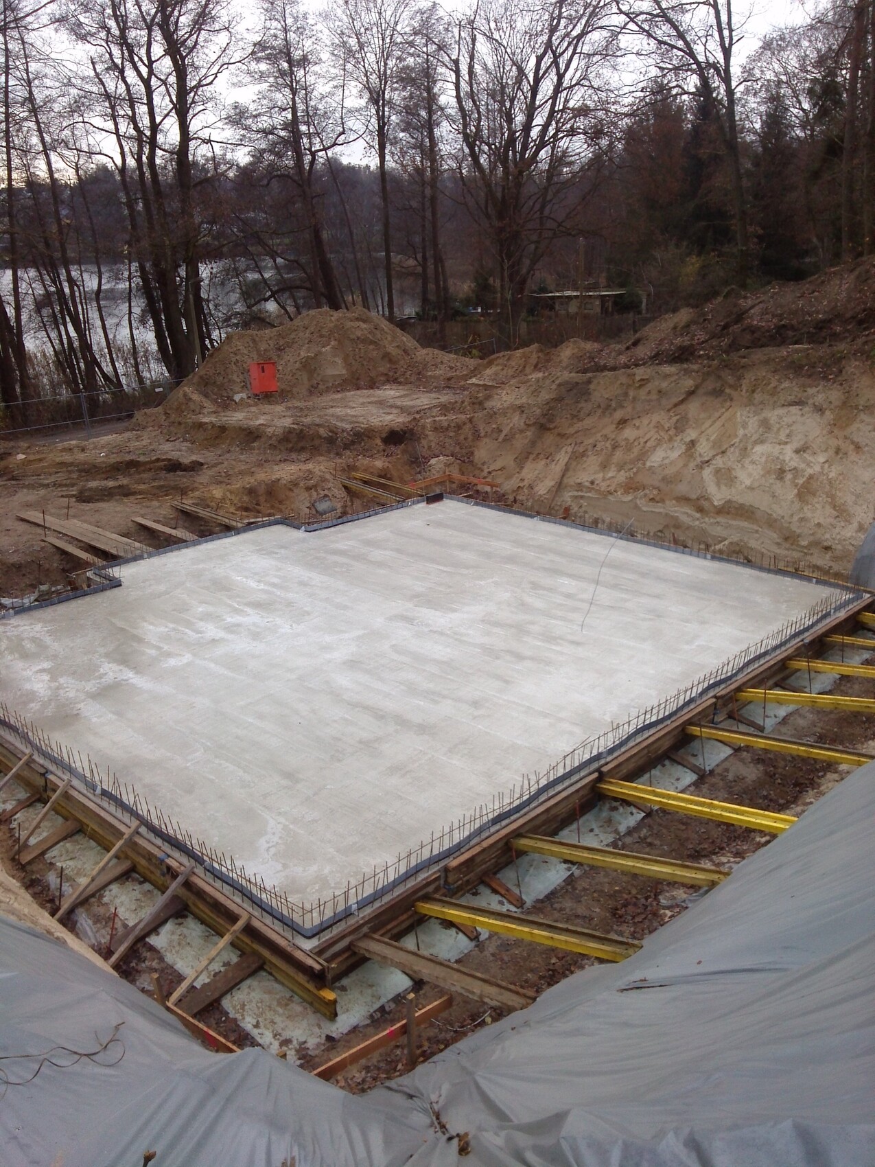 Gegossene Betonfundamentplatte in Baugrube, Bewehrung am Rand, Erde drumherum.