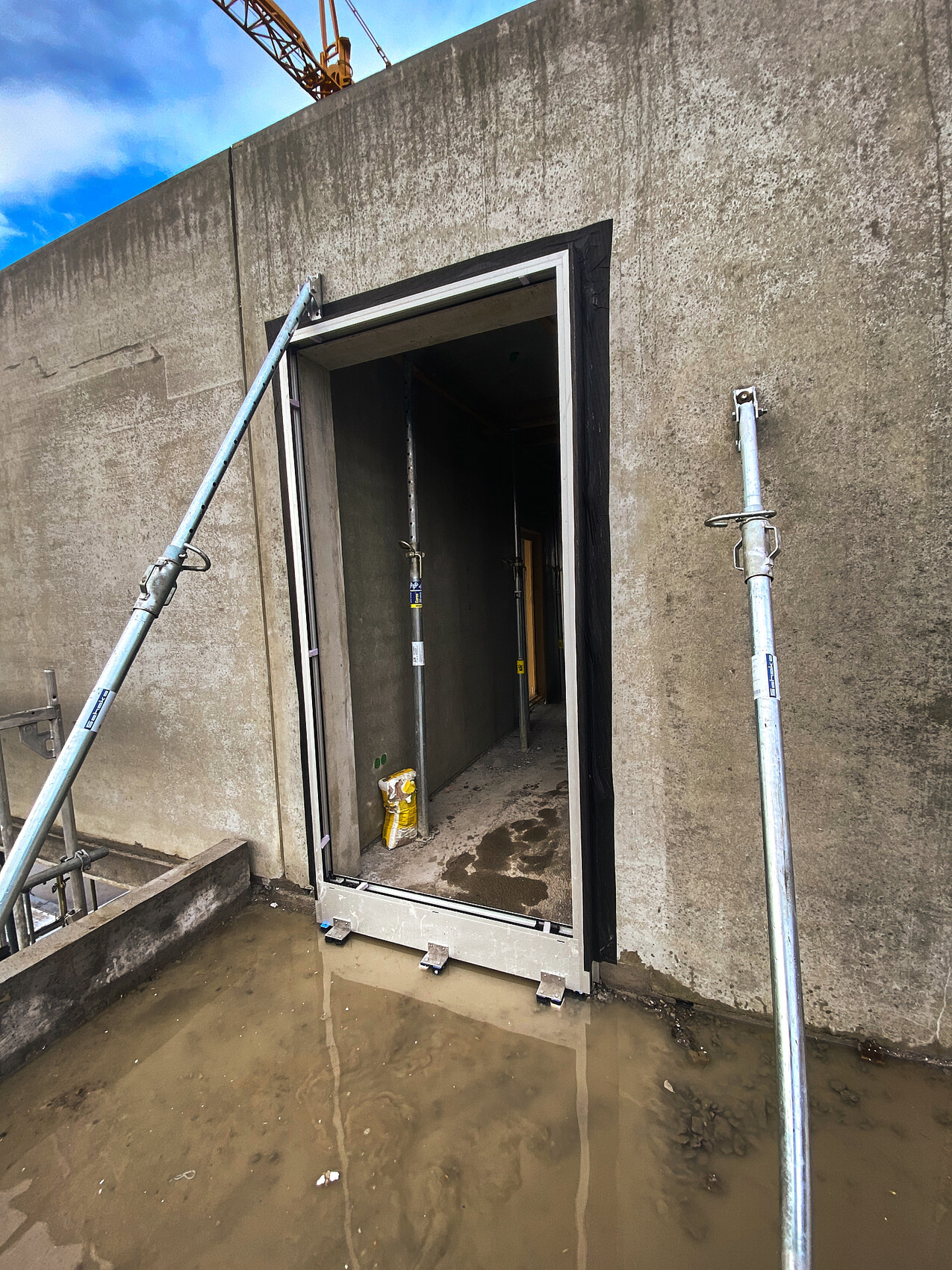 Open doorway in a concrete wall at a construction site, scaffolding poles next to it, puddle in front.