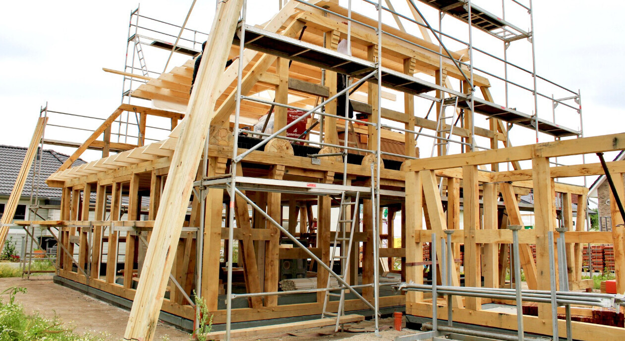 Wood frame construction of a building in the shell stage, with scaffolding and construction timber on site.