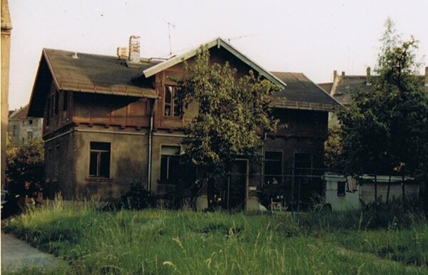 Two-story old house with a tree in the front yard and grass in front.