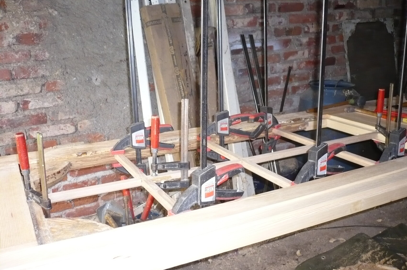Wood frame construction in workshop; clamps hold wooden beams together in a frame.