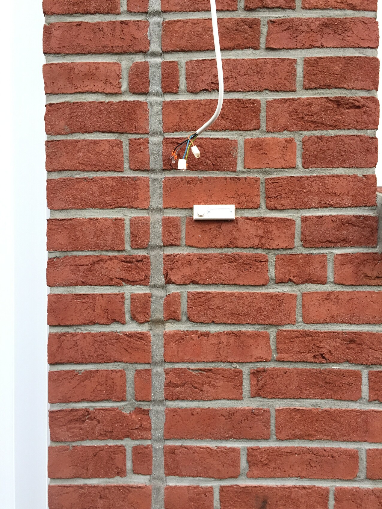 Aussenwand aus roten Ziegeln mit freiliegendem Elektroanschluss und Kabeln