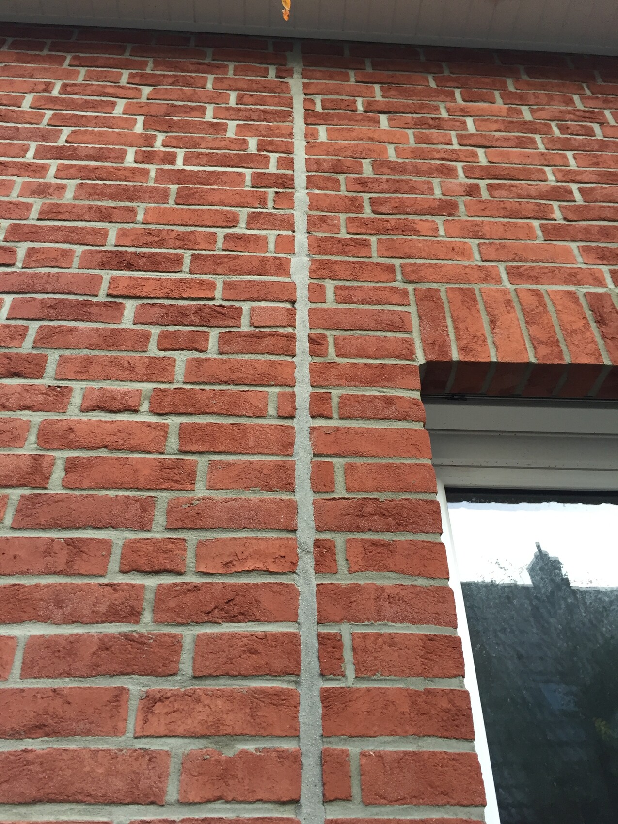 Rote Backsteinwand mit senkrechter Fuge, unten rechts Fenster mit dunklem Glas.