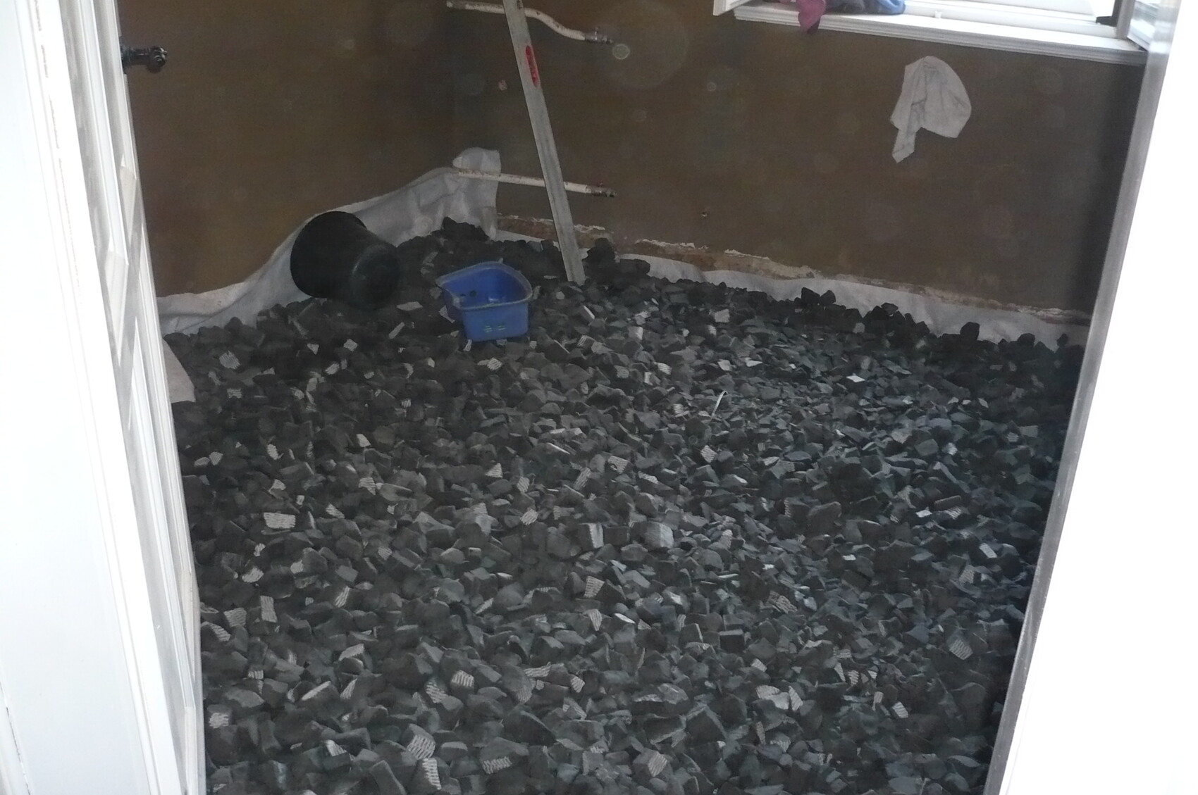 Room full of dark pebbles on the floor; blue plastic box, black bucket, and metal rod.