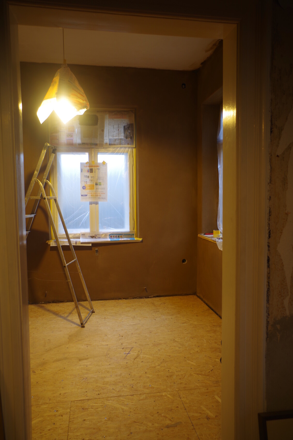 Renovation room with ladder, temporary lighting, and window covered with plastic.