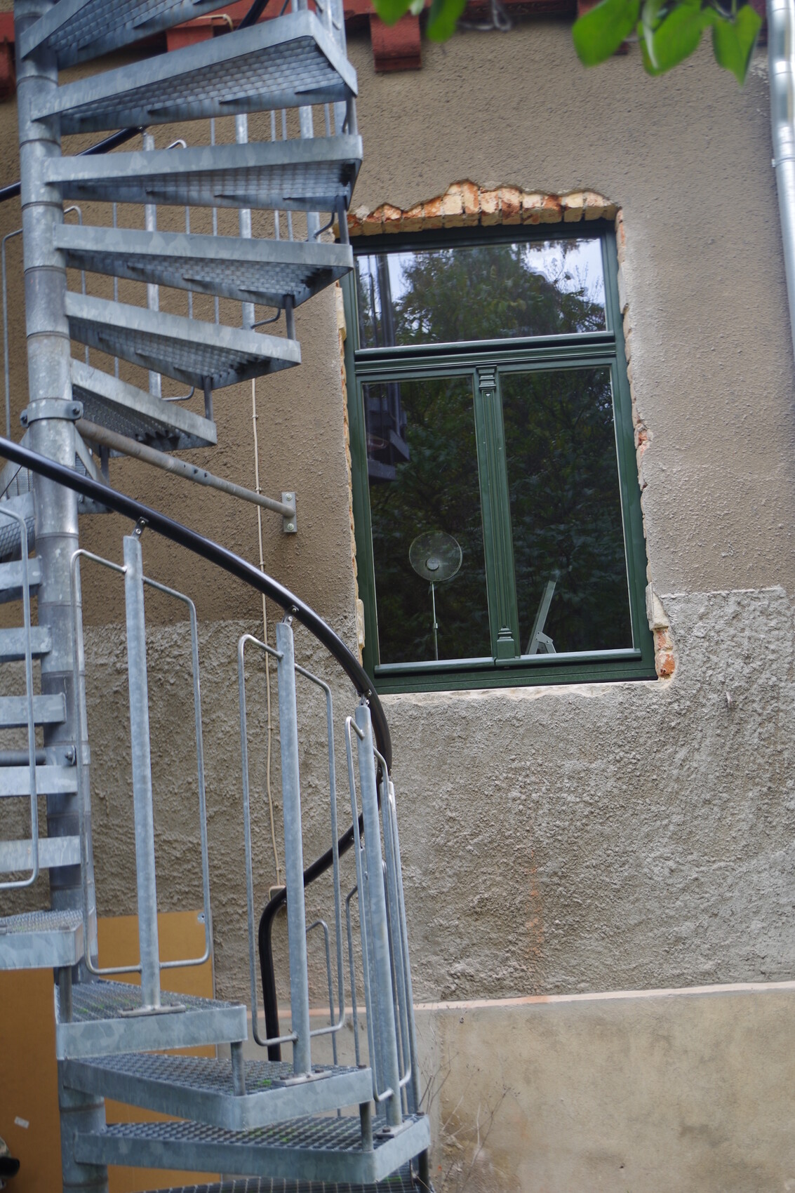 Metal spiral staircase on the building next to a green window, crumbling facade visible.