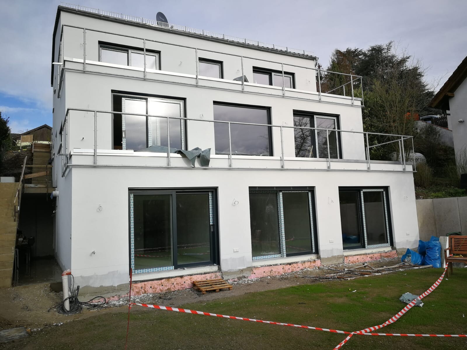 Modern white residential house with large windows and balconies; construction site in front.