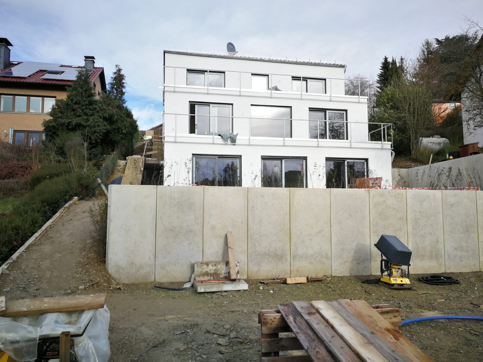 White modern villa on hillside with large windows; construction equipment in foreground.