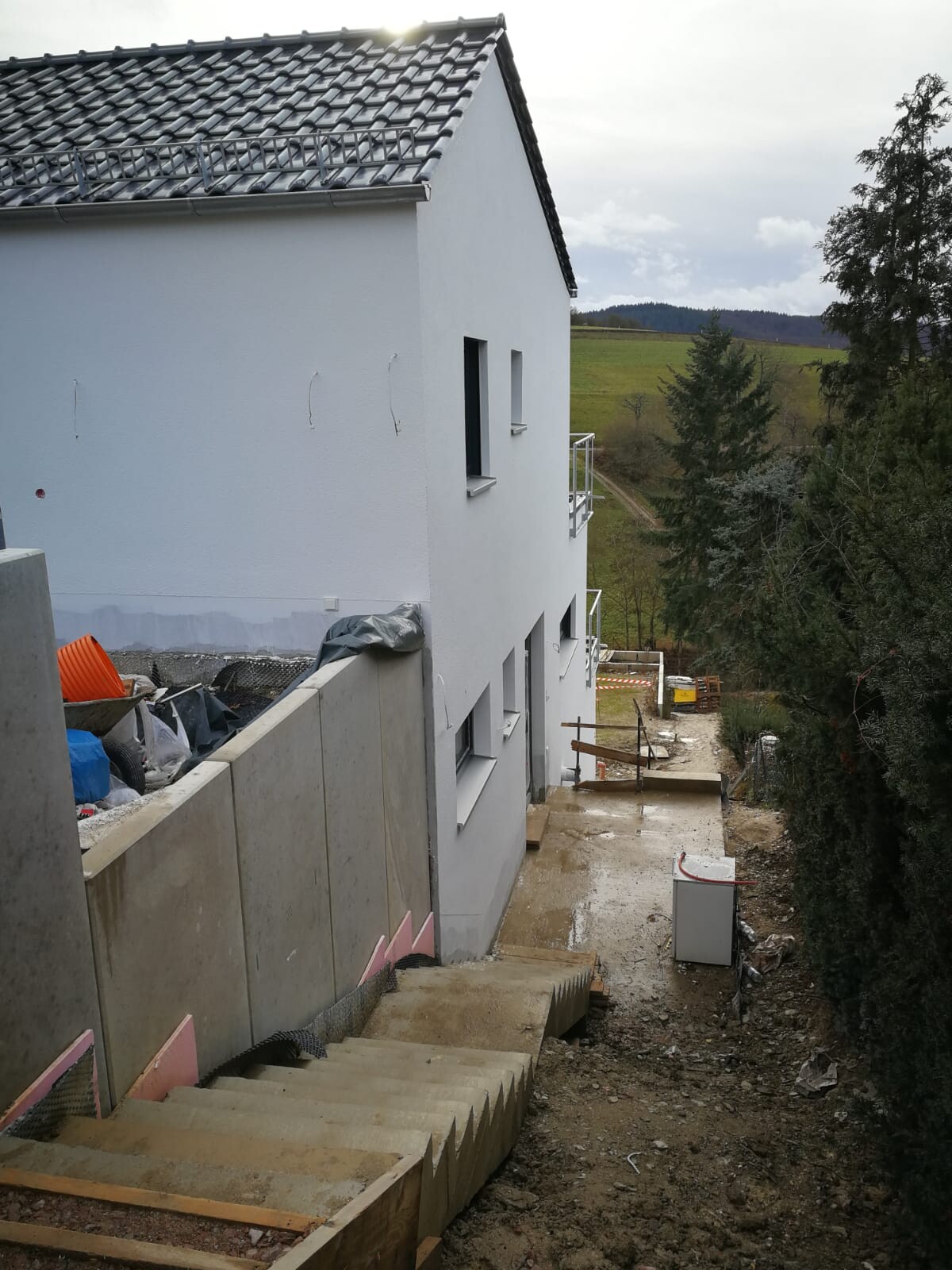 White house on hillside with construction work: concrete steps, construction waste and landscape in background.
