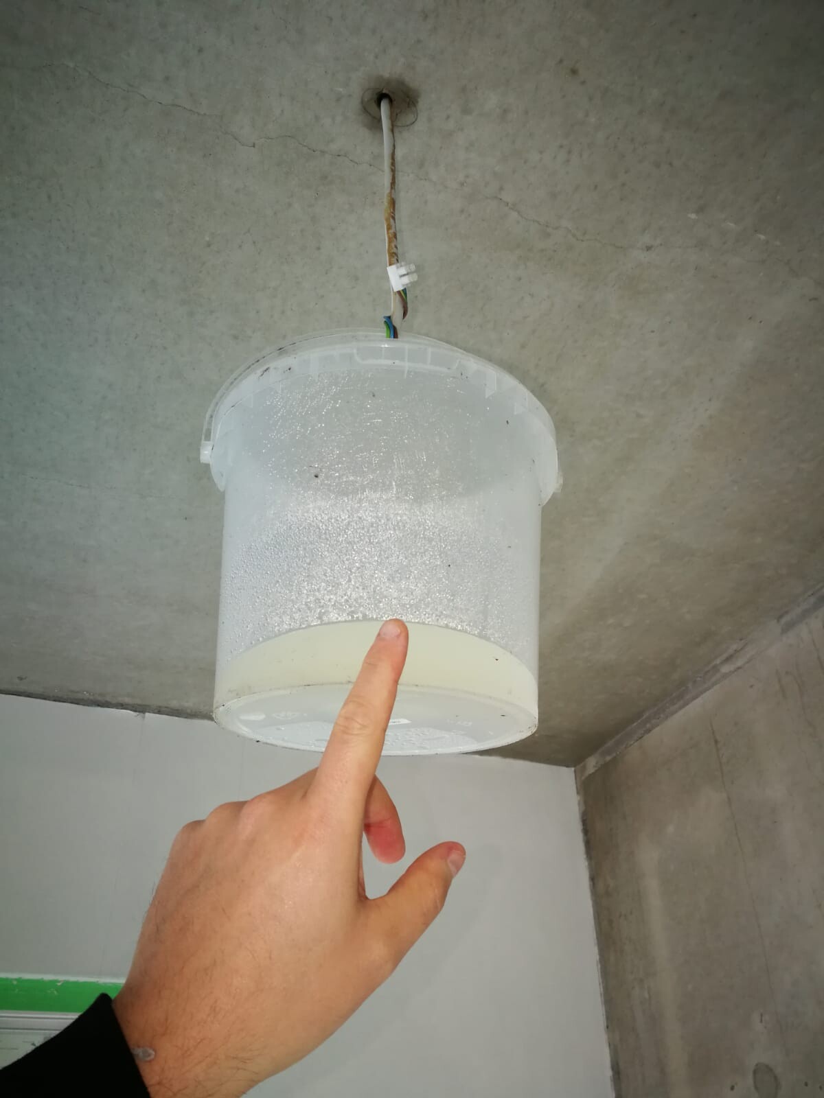 Suspended milky cylindrical ceiling light under a concrete ceiling; finger pointing at it.